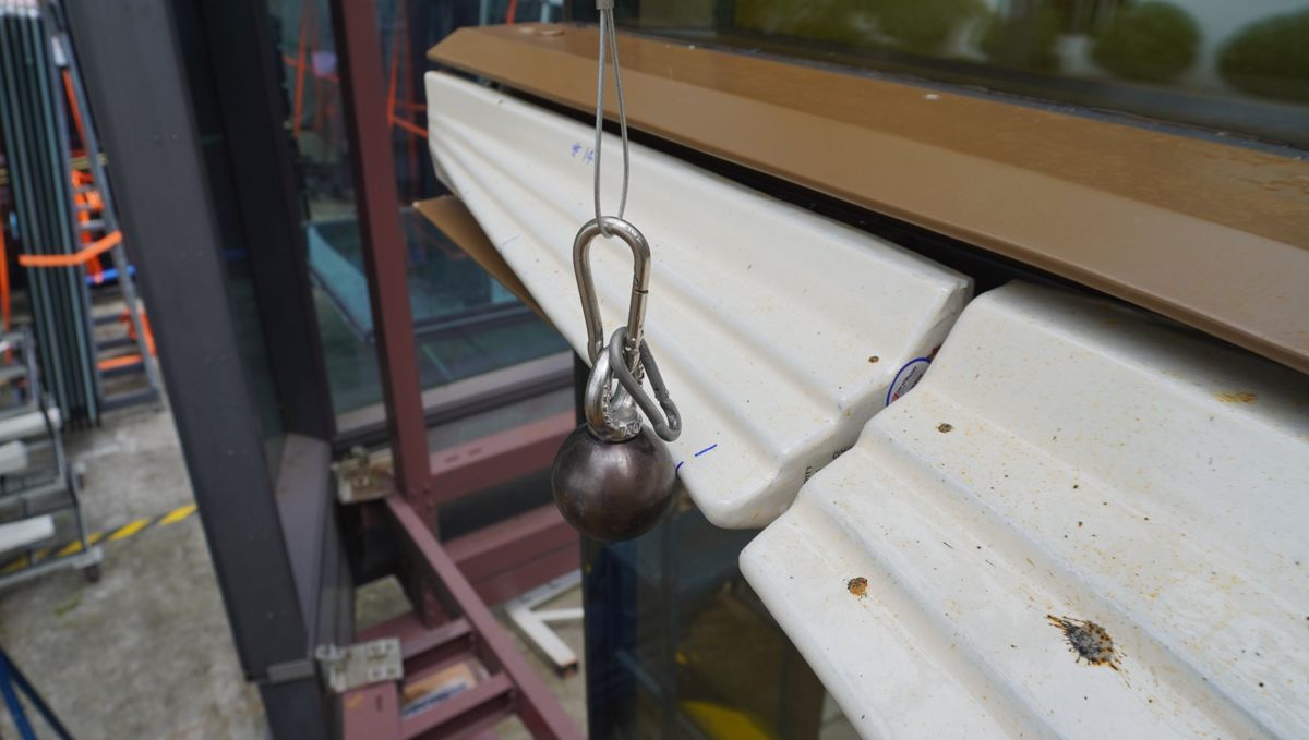 Steel ball hard-body impactor suspended in front of terracotta tile cladding